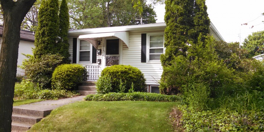 Exterior of a home with white siding, black shutters, and covered front entry.