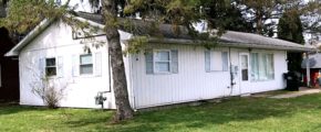 Exterior of ranch house with small lawn, light vertical siding, and pale blue shutters.