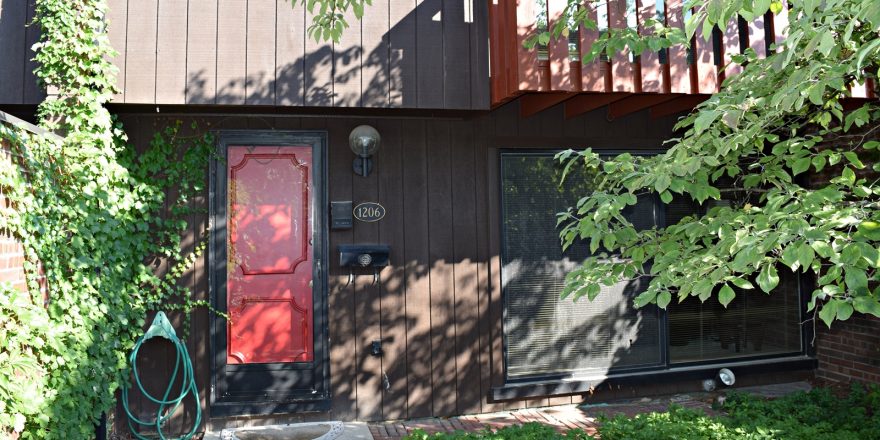 Exterior of a townhome with a bright red front door and brown large-panel siding