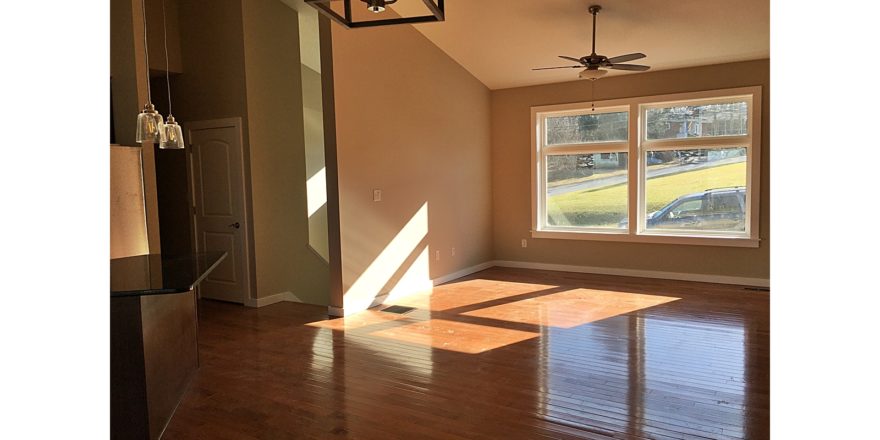 Living room with vaulted ceilings, hardwood floors, large picture window, and ceiling fan