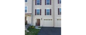 Exterior of townhouse with light tan siding and maroon front door and shutters