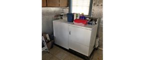 Laundry room with side-by-side top load washer and front load dryer with cabinets perpendicularly above.