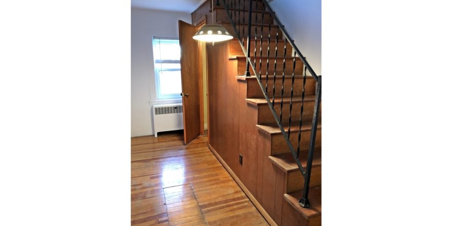 Wooden stair case with hanging light and hardwood floor.