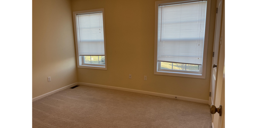 an empty room with two windows and carpet