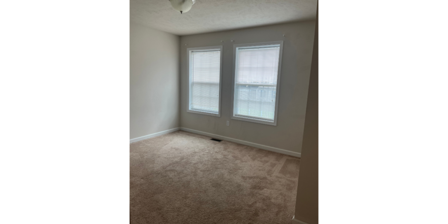 an empty room with two windows and carpet