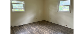 an empty room with two windows and a hard wood floor