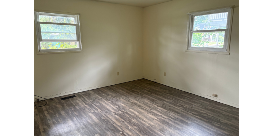 an empty room with two windows and a hard wood floor