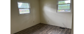 an empty room with two windows and a hard wood floor