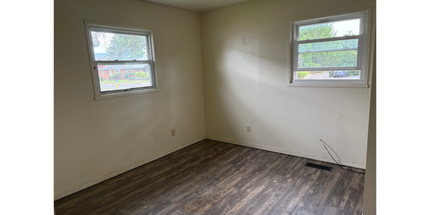 an empty room with two windows and a hard wood floor