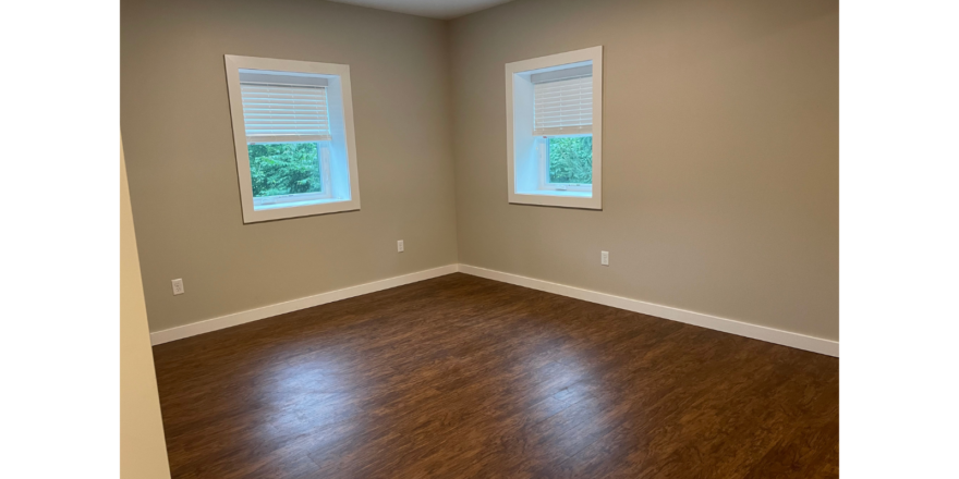 an empty room with two windows and a hard wood floor