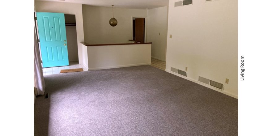 Large, carpeted living room with teal door and pendant light over a stairwell