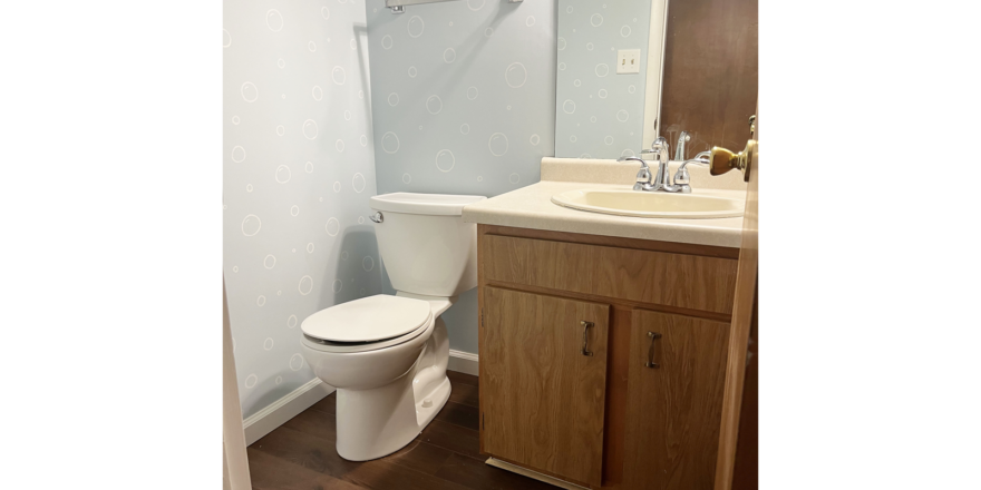 an off-white toilet sitting on dark wood flooring next to an off-white bathroom sink with chrome fixtures and dark wood vanity