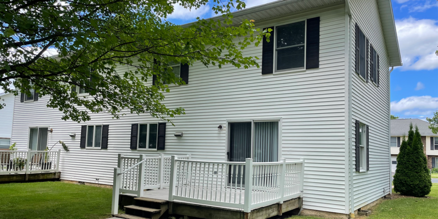 Duplex with white siding, black shutters, a garage, and gray shingles, and a back porch