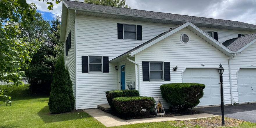 Duplex with white siding, black shutters, a garage, and gray shingles