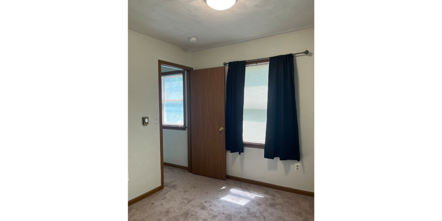 an empty room with a door, carpet, and a window