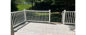 a wooden deck with white railings and trees in the background