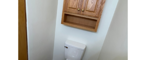 a bathroom with a toilet and wooden cabinet above it